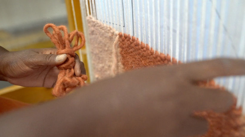 hands weaving a pink rug 